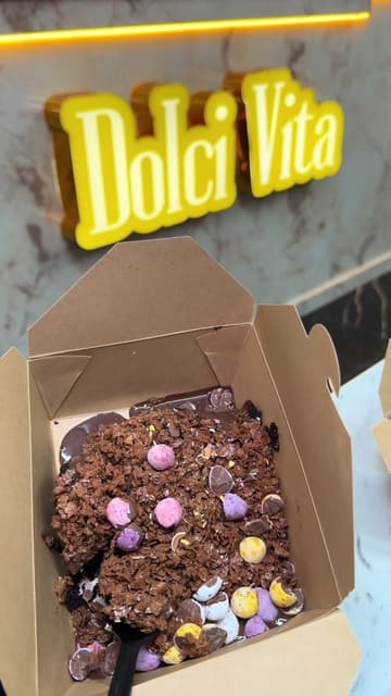 A promotional video showcasing a range of Mini Egg-themed desserts at Dolci Vita, including brownies, cakes, and waffle balls, with a clear view of the menu.