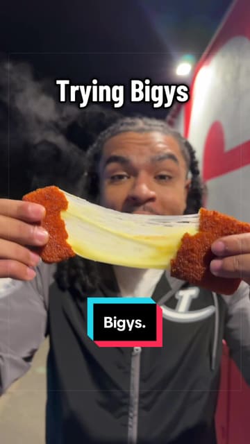 A creator reviews various menu items from Bigys in Ilford, including a cheese stick, loaded mac and cheese, a burger, and a dessert. The video features the creator's enthusiastic commentary and close-up shots of the food, highlighting the indulgent nature of the dishes.