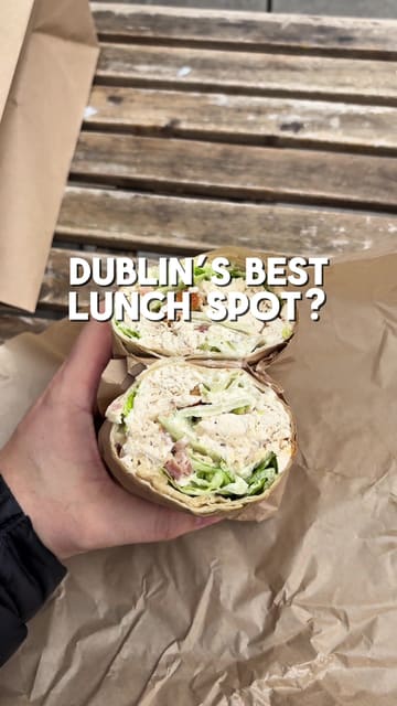 The creator visits Mrs. Reid's in Dublin to review their lunch offerings, specifically a chicken caesar wrap and a breakfast roll. The video features the creator talking to the camera, showing the exterior and menu, and providing a taste test of the food.