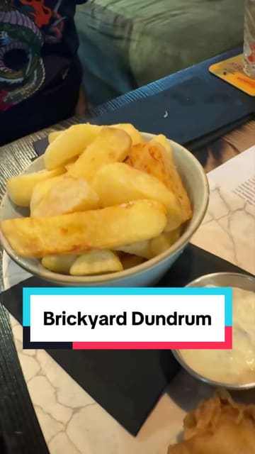 The video is a first-person review of Brickyard, a gastropub in Dundrum. The creator walks through the beer selection, showing the menu board and a beer flight, followed by a montage of various dishes including nachos, mac and cheese bites, wings, a burger, steak, and fish and chips. The creator provides commentary on the quality of the food and the beer selection.