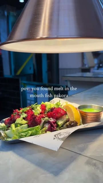 A short, casual video showcasing fish pakora at a street food venue, featuring a close-up of the dish being prepared with lemon and a quick shot of the menu board.