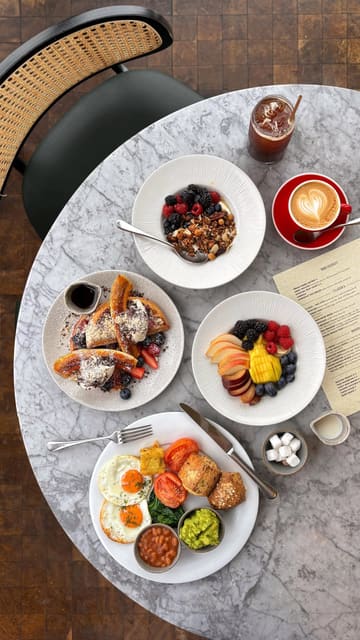 A high-quality, aesthetic showcase of a breakfast spread at a high-rise restaurant in London, featuring iconic skyline views and signature dishes like waffles and a full English breakfast.