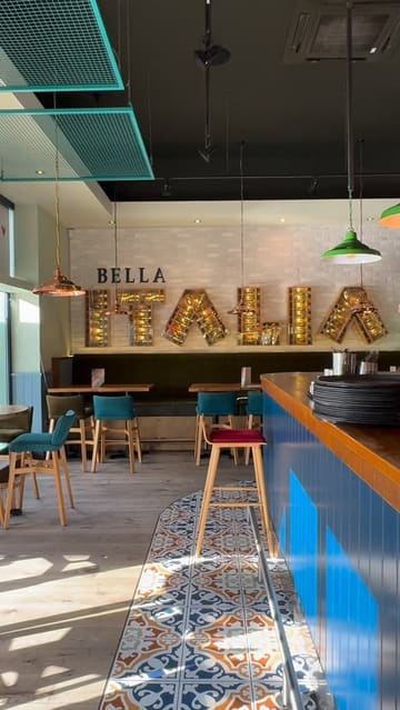 A montage-style video showcasing a visit to a Bella Italia restaurant, highlighting the interior, various pasta dishes, a cocktail, and the use of a robot server to deliver food.