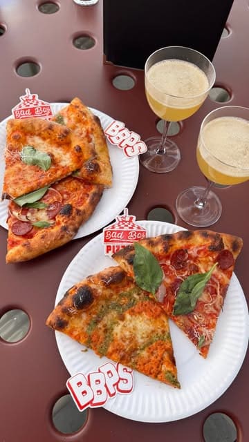 An overhead, flat-lay style shot of pizza slices and drinks served on a metal mesh table at a rooftop venue.