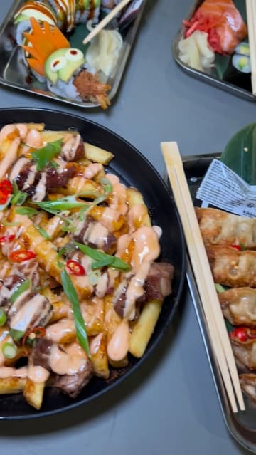 A short, energetic vlog featuring a visit to Inamo Sukoshi at Kargo Mkt. The video showcases the venue's atmosphere and highlights specific dishes including duck loaded fries, sushi rolls, and gyoza, with the creator trying the food on camera.