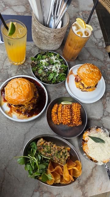 A high-quality, fast-paced montage showcasing a variety of dishes at Burger & Beyond, including burgers, steak tartare, corn ribs, and dessert, with close-ups of food preparation and consumption.