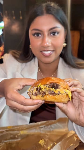 A short video featuring a creator trying the smashed onion double cheeseburger at Flat Iron, followed by a shot of a steak being drizzled with sauce.