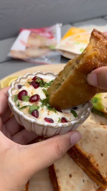 A short video showcasing an Indian-inspired sharing board created using 'Tuk In' pre-packaged food products, including various samosas and 'Curry in a Naan' items, served with chutneys.