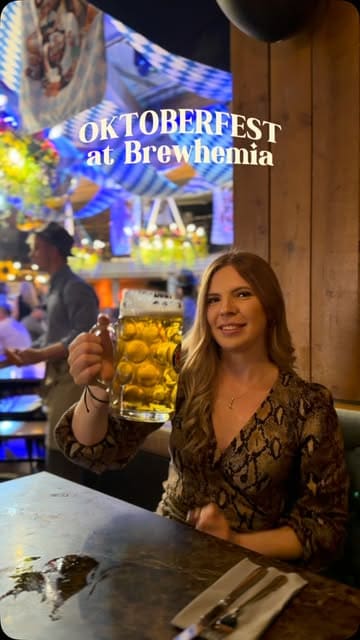 A vibrant vlog-style reel showcasing an Oktoberfest event at Brewhemia. The creator highlights the festive atmosphere, live entertainment, and traditional German food and drink, including pretzels, currywurst, and schnitzel.
