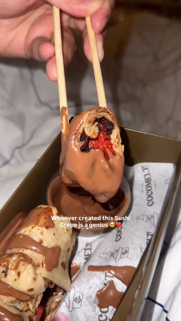 A short, handheld video showcasing a 'sushi crepe' dessert from Cocomelt London, featuring a close-up of the crepe being dipped into chocolate sauce.