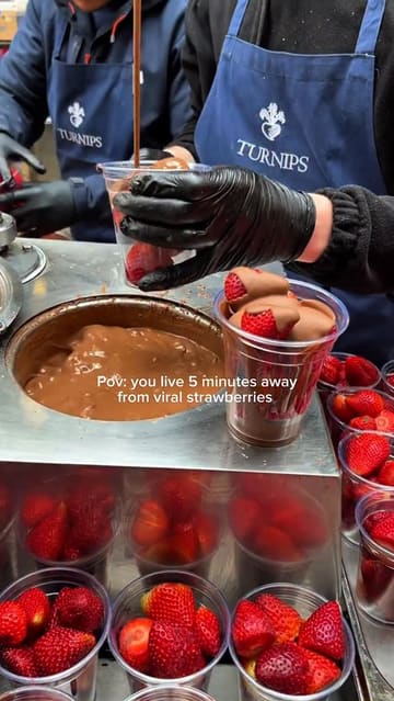 A short, high-quality clip capturing the preparation of chocolate-covered strawberries at a market stall in Borough Market, London. The video focuses on the dipping process, highlighting the fresh fruit and rich chocolate coating.