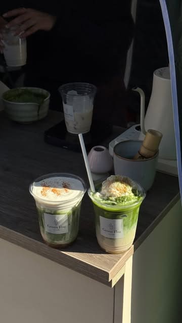 A short, aesthetic video showcasing unique matcha drinks from the Green Flag Club pop-up stall at a market. The video features close-up shots of the preparation and final presentation of banana pudding, apple spice, and rose matcha drinks.