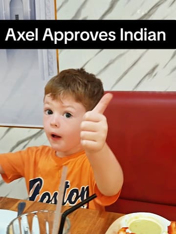 A family vlog documenting a dinner experience at D’Feringghi Tandoori House in Penang, Malaysia. The video features the parents and their young son, Axel, trying various Indian dishes including tandoori chicken, rogan josh, and cheesy garlic naan. The content focuses on their genuine reactions and the child's approval of the food.