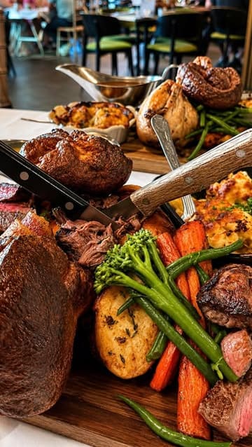 A montage video showcasing a Sunday roast dining experience at The Grand Hotel in Swansea, featuring close-ups of a large sharing platter, gravy pouring, and desserts.