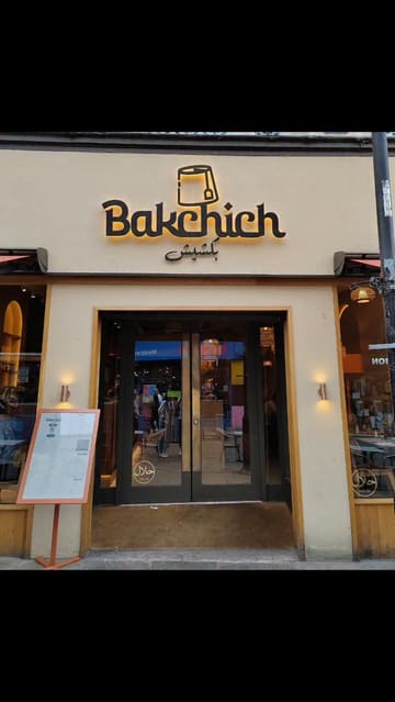 A visual tour of Bakchich, a Lebanese restaurant, featuring shots of the exterior, the menu, and various dishes including spring rolls, hummus, halloumi tacos, and a mixed grill platter, set to music with text overlays.
