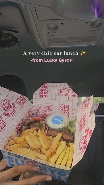 A short, handheld vlog-style video showcasing a takeaway meal from Lucky Gyros, eaten in a car. The creator displays various items including a lamb kofta gyro, rice boxes, and a platter, accompanied by a drink.