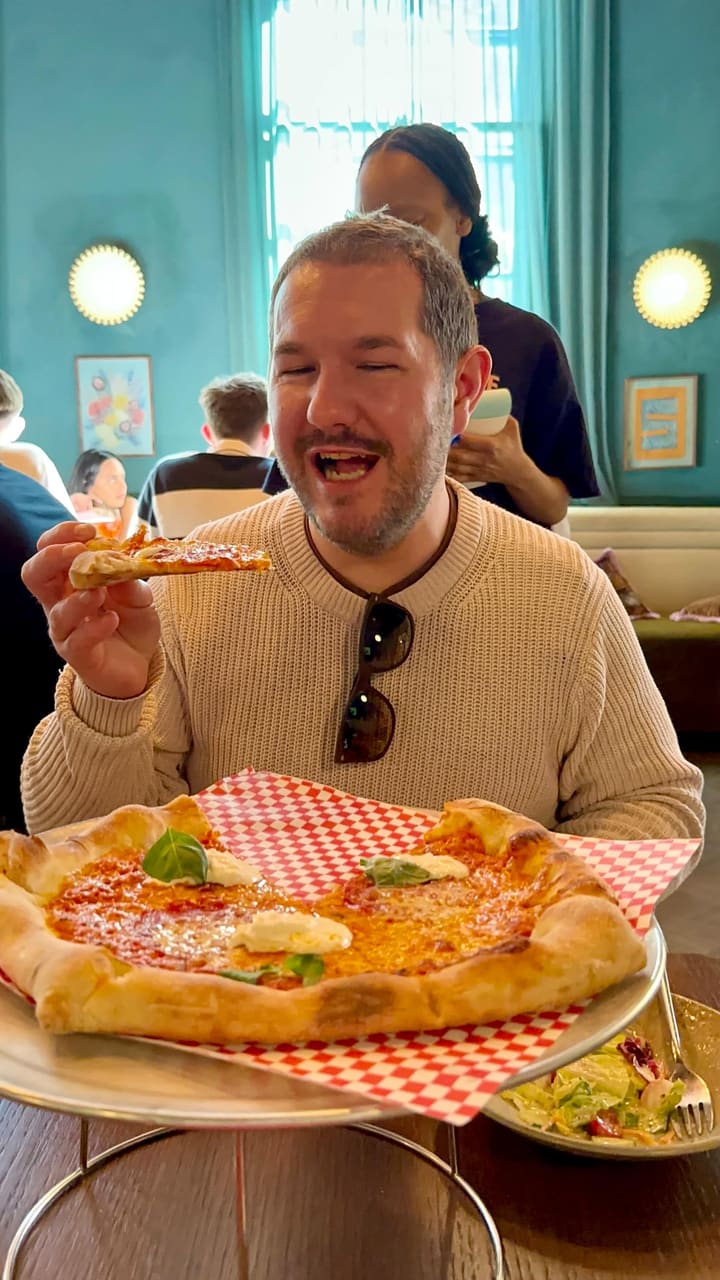 The video promotes an unlimited pizza brunch at Eve X Proper Slice, located in a hotel near Earls Court, London. It features close-ups of various pizzas, including pepperoni and a vegetable-topped pizza, a side salad, and a cocktail. The video emphasizes the unlimited pizza offer for £20 per person for 90 minutes and highlights that selected cocktails are available for £5. It shows individuals enjoying the pizza and provides glimpses of the venue's exterior and interior.