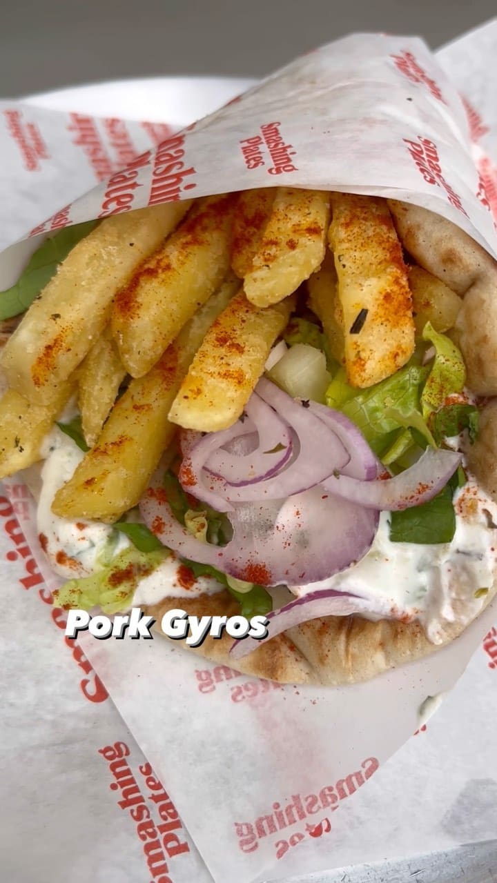 This video showcases Smashing Plates, a Greek street food restaurant in London. The video features various food items including Lamb & Beef Naked Souvlaki with a Greek salad, Pork Gyros, Halloumi Bites, fries with oregano salt, Chicken Bites, and Pitanuts (a cinnamon-sugar pita bread). The food is presented on Smashing Plates branded paper. The video emphasizes the speed and convenience of ordering through a screen.
