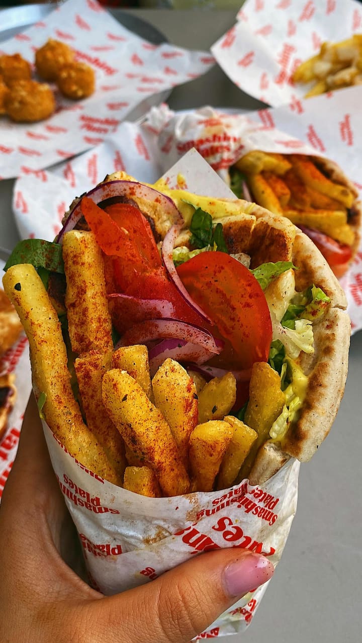 The video showcases Smashing Plates, a Greek street food vendor in London. It highlights various menu items, including souvlaki wraps with halloumi and fries, pitanuts (pitta donuts with chocolate sauce), and a Greek salad. The food is presented in visually appealing ways, emphasizing its freshness and tastiness.  The video also showcases the self-service kiosks and mentions that veggie/vegan options are available. The primary focus is a meal showcase, with the influencer enthusiastically endorsing the food.