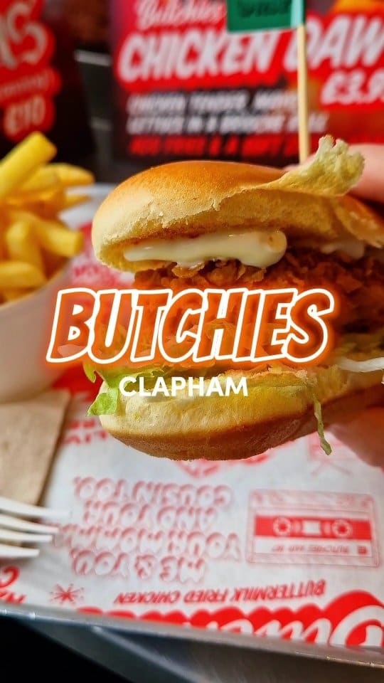 This video reviews a £3.95 chicken dawg from Butchies in Clapham, London. The video shows close-up shots of the sandwich, fries, and a Red Leicester dipping sauce. The reviewer takes a large bite, showcasing the cheese pull, and gives a thumbs-up.