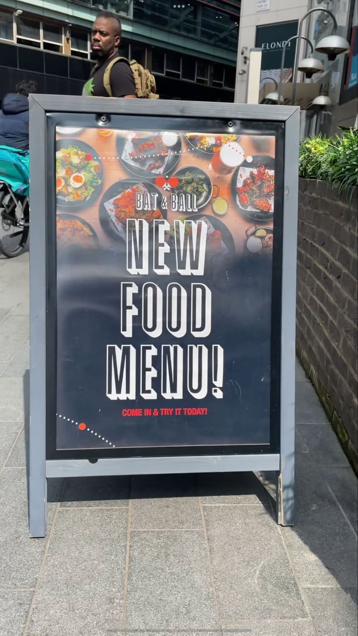 The video showcases Bat & Ball, a bar in Stratford, East London. It features various food items including pizzas (BBQ Pollo), burgers (Frying Nemo), crispy squid, Korean chicken wings, churros, and cheesecake. The drinks shown are cocktails (Zombie and Lady Luck) and beers (Guinness). The video also displays the venue's interior, including table tennis and pool tables, and shows a bartender making a cocktail.