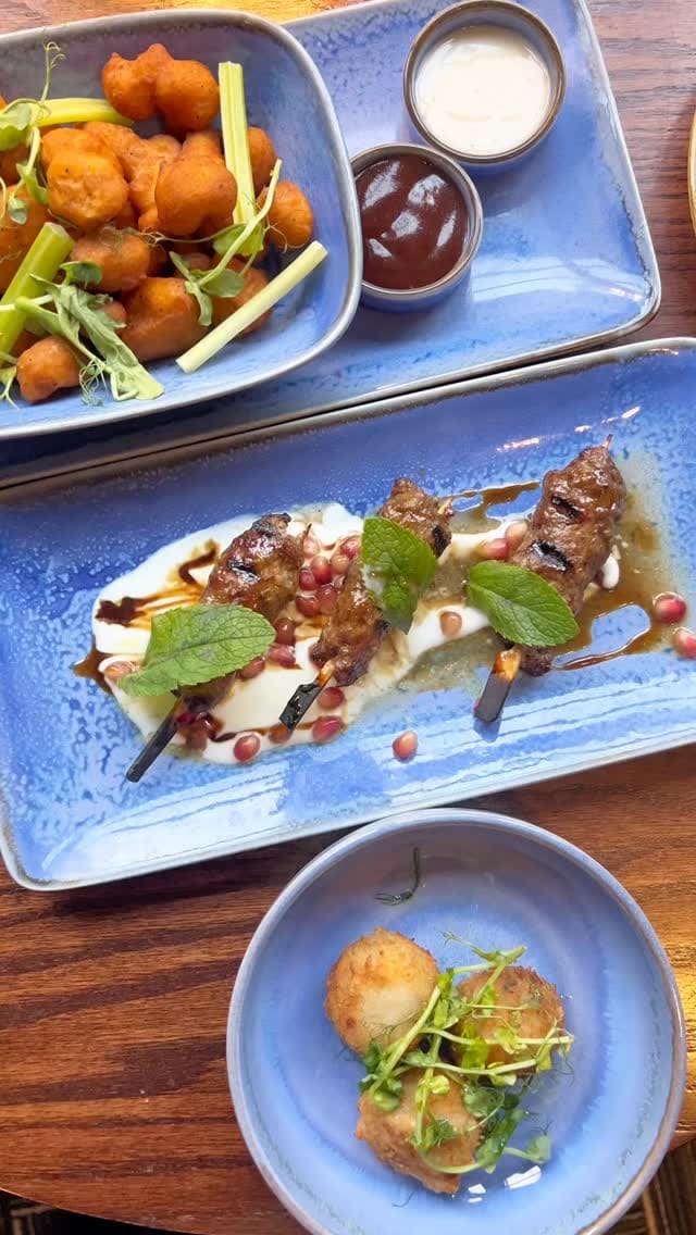 A video montage showcasing a meal at Archy's restaurant, located in the Marble Arch Hotel. The video displays a variety of dishes, including small plates like crispy cauliflower bites, lamb kofta, and mushroom arancini. It also features main courses such as a plant-based burger, a superfood salad, spaghetti, and a stone-baked pizza. For dessert, a New York-style cheesecake is shown. The video includes shots of the restaurant's cozy and stylish interior, a grand piano, the bar, and two people toasting with mocktails.