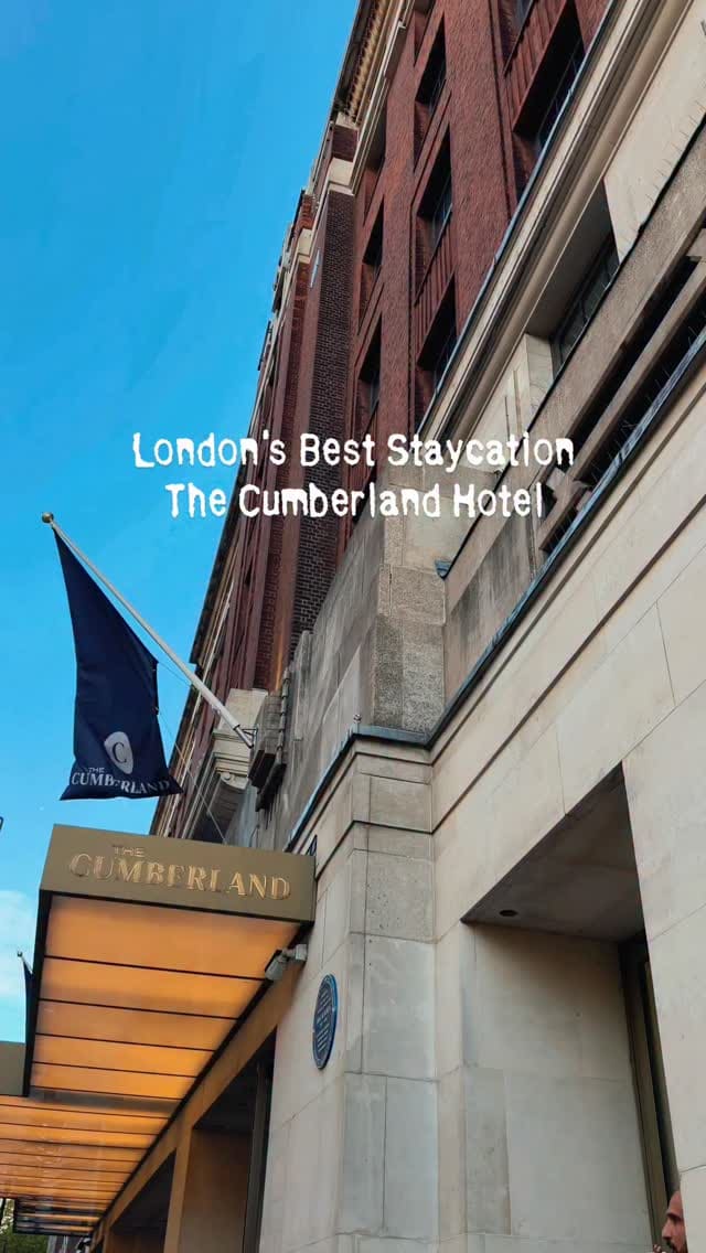 This video is a promotional montage for The Cumberland Hotel in London. It showcases various aspects of a stay, beginning with an exterior shot of the hotel. It then moves inside to a music-themed bedroom with a guitar and a record player. The video highlights amenities like a welcome card, a fruit platter, and rosé champagne. It also features scenes from the hotel's bar with a colourful cocktail, a live music performance, and an extensive breakfast spread including pastries, an omelette, waffles, and pancakes. The video concludes with shots of the express checkout, an on-site Starbucks, and the nearby Marble Arch landmark.