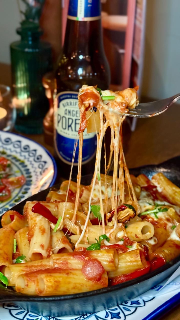 The video promotes the opening of a new Prezzo Italian restaurant in Edinburgh. It showcases the restaurant's exterior and modern interior, followed by close-up shots of several vegetarian dishes. The food featured includes gooey mozzarella sticks, creamy burrata being cut open, rigatoni arrabbiata al forno with a cheese pull, a margherita pizza, and a slice of custard cream tiramisu.