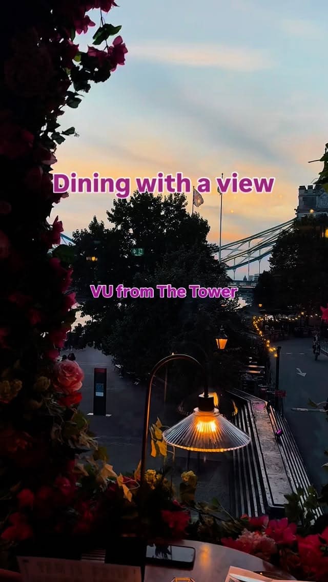 A video montage showcasing a dining experience at 'VU from The Tower' restaurant in London. The video highlights the stunning sunset view of Tower Bridge from the restaurant window. It features clips of two people toasting with colorful cocktails, the restaurant's interior and bar area, and various dishes being served and eaten. The food shown includes arancini being cut open, a steak with chips and kale, a cheese pizza, and popcorn chicken.