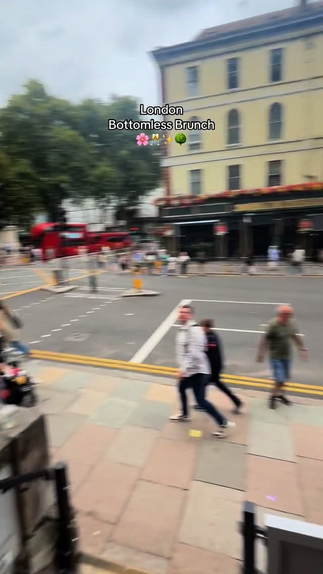 A video showcasing a bottomless brunch experience at 'The Soak' restaurant in London. The video begins with a couple taking a selfie in front of the venue's floral entrance, then shows the stylish, flower-adorned interior. It features clips of the menu, sparkling wine being poured, and a variety of dishes being served. The food shown includes popcorn chicken, salt and pepper squid, a chicken katsu curry with edamame beans, a chicken burger with fries, and sides of broccoli and salad.