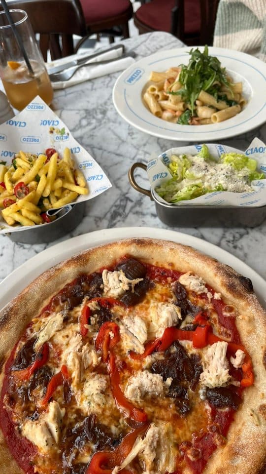 The video showcases a meal at the newly refurbished Prezzo Italian restaurant in Nottingham. It begins with an exterior shot, then moves inside to show a variety of dishes and drinks. The items featured include cocktails, dough balls with dip, fried mozzarella sticks with a prominent cheese pull, a pasta dish being topped with freshly grated parmesan, a pizza, seasoned fries, a Caesar salad, and two desserts, one of which is a chocolate dish with ice cream.