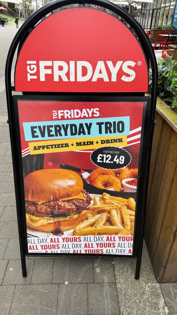 The video is a vlog-style review of a TGI Fridays restaurant. The creator walks through the venue, highlighting the interior decor, the 'Everyday Trio' value menu offer, and samples several dishes including chicken, pasta, fajitas, and dessert, paired with an espresso martini.