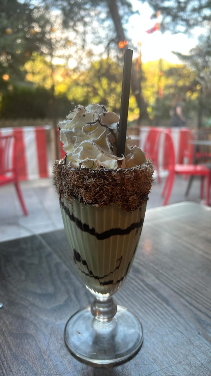 The video promotes the new "Dubai Chocolate Shake" at a TGI Fridays restaurant. It begins with an exterior and interior shot of the restaurant. The main focus is on the shake, showing it from various angles and highlighting its ingredients (pistachio cream, kataifi pastry, whipped cream, chocolate sauce) with text overlays. A person is shown drinking the shake. The video also briefly showcases a S'mores Sundae and a bag of popcorn before ending with a final shot of the main shake.