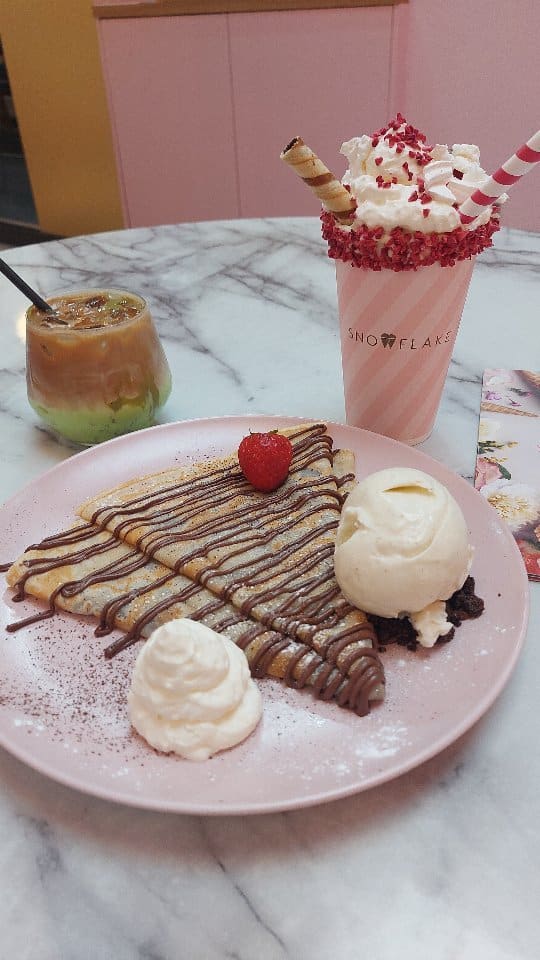 The video showcases Snowflake Gelato in Soho, London. It features crepes with Nutella, whipped cream, and vanilla ice cream; a strawberry and cream sundae shake; and an iced pistachio latte. The presentation is visually appealing, with pastel colors and a focus on the dessert's textures and details.  The video highlights the use of 100% natural ingredients and organic Jersey milk and cream.
