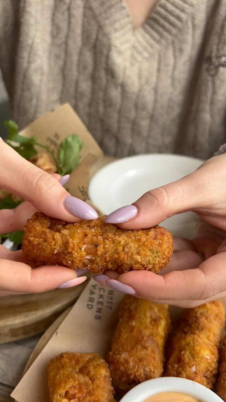 This video showcases a Sunday roast meal at 197 Chiswick Fire Station.  It begins with a close-up of Nduja and Cheddar croquettes being pulled apart, showing the cheese pull.  Then it shows dipping a croquette in sauce. Next, it shows a passionfruit drink, followed by several plates of roast dinners with various meats (beef, chicken, pork), roast potatoes, Yorkshire puddings, gravy, and vegetables. Finally, it shows an apple and raspberry crumble with ice cream and a mango sorbet. The food is presented attractively, and the setting appears to be a modern, upscale restaurant.