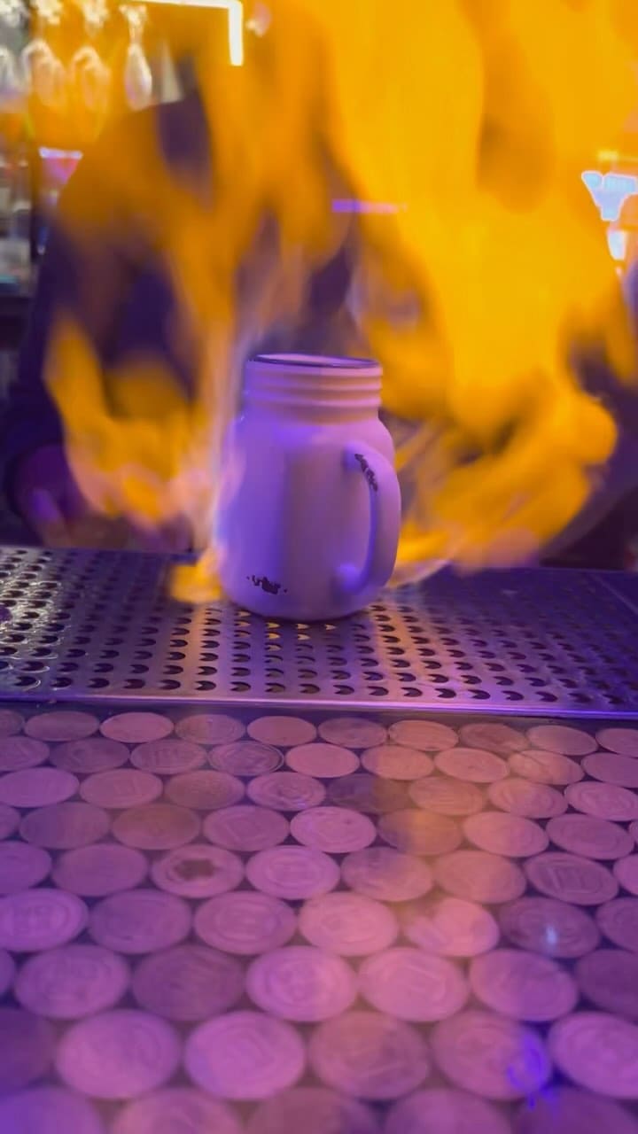 The video showcases NQ64, an arcade bar in Shoreditch. It features various cocktails (including one that's set on fire), and a wide array of arcade games, from retro classics to modern titles like Guitar Hero and Top Skater. The presentation emphasizes the vibrant atmosphere and fun, social aspects of the bar.