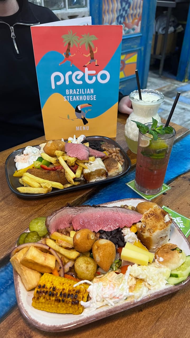 This video promotes Preto, a Brazilian Rodizio restaurant in the West End. The video showcases the unlimited Brazilian BBQ experience, featuring various cuts of meat such as lamb, beef, chicken wings, ribs, and Brazilian sausages, all carved in front of the customer. It also highlights the unlimited buffet with traditional dishes like Feijoada, Coxhinhas, and Pao de Quejo, along with salads and dips. The video also shows desserts like Brigadeiro, chocolate cake and flan. Drinks are also shown. The main focus is on the unlimited Rodizio grill and the variety of food offered.