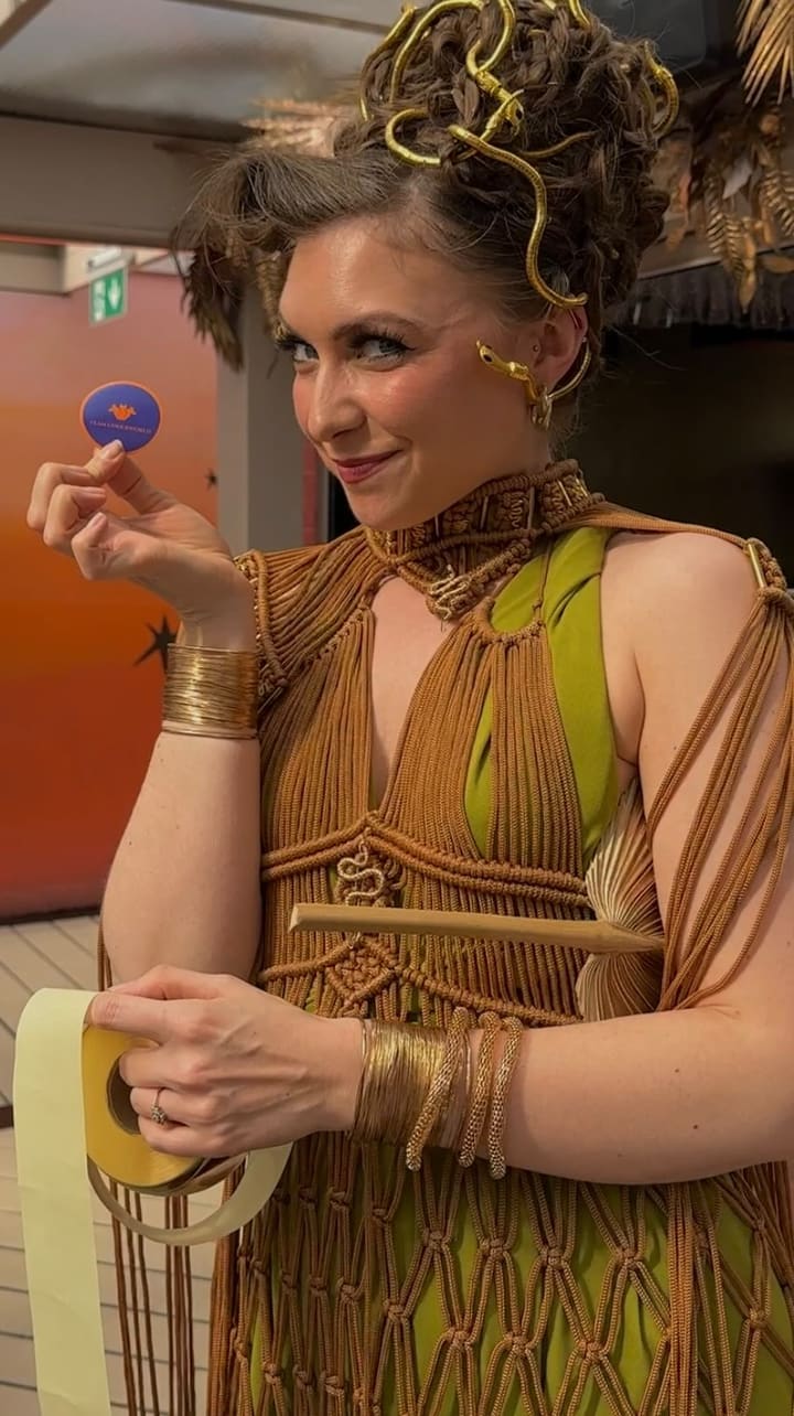 The video promotes a 'Clash of the Gods' themed bottomless brunch event at Circe's rooftop. It features attendees and performers dressed in Greek mythology-inspired costumes, showcasing live performances, interactive games like Jenga, and scenes of people enjoying bottomless drinks such as prosecco and cocktails. The video also briefly shows brunch dishes including pita bread with toppings and fries, highlighting the lively and chaotic atmosphere of the event.