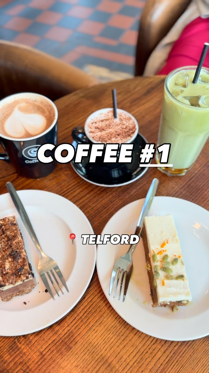 A promotional video for Coffee #1 in Telford. The video showcases the cafe's exterior and spacious, book-themed interior. It features close-up shots of various drinks, including a latte with heart-shaped art, a babyccino, and an iced matcha latte. Two cakes are also highlighted: a chocolate slice and a carrot cake slice with pumpkin seeds. The video includes shots of the cafe's decor, such as a world map and bookshelves, and a clip of a barista pouring milk to create latte art.