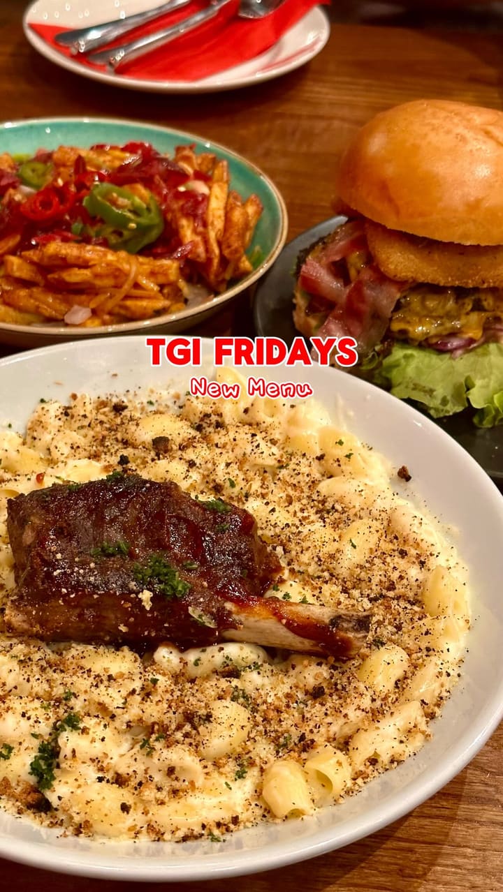 The video is a promotion for the new food and drinks menu at a TGI Fridays restaurant. It showcases a full dining experience, starting with cocktails (a blue Raspberry Ripple and an orange Soaber Loader), moving to appetizers (Tex-Mex Nachos and Mozzarella Planks with a cheese pull), then main courses (an Ultimate Cheese Dipper Burger and Beef Short Rib Mac & Cheese), and finishing with desserts (Pecan Pie and a Salted Caramel & Chocolate Brownie Sundae). The video includes close-ups of the food, shots of the creators enjoying their meal, and views of the restaurant's interior and exterior.