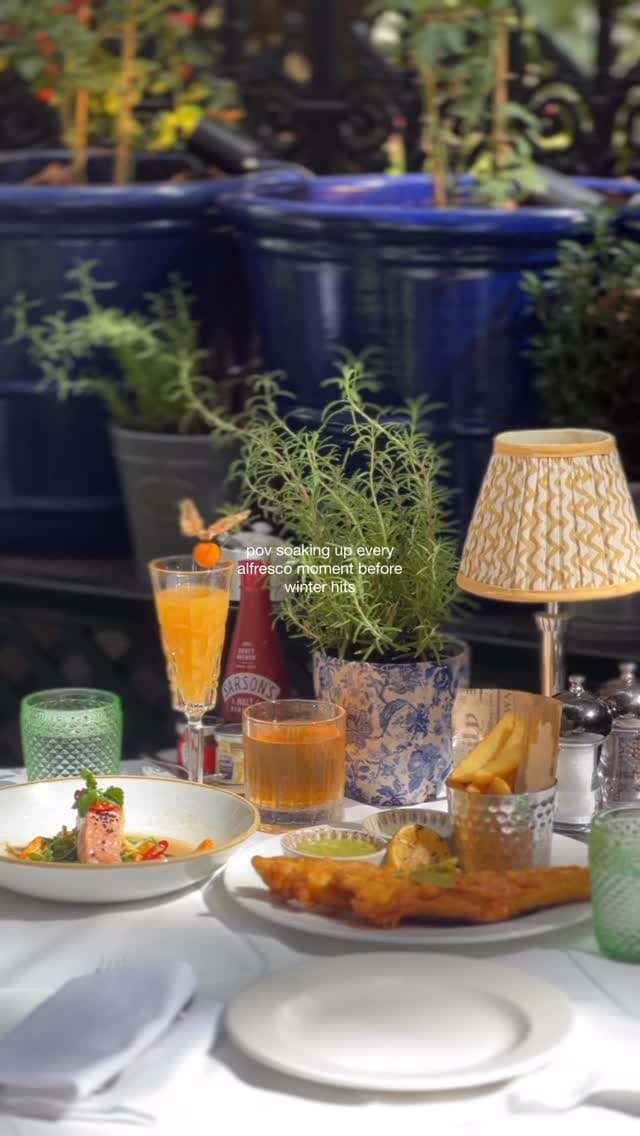 A short, aesthetically pleasing video showcasing an alfresco dining experience at The Terrace at The Royal Horseguards hotel in London. The video features various shots of the beautifully decorated terrace, a table set with dishes including fish and chips and miso-glazed salmon, and two cocktails. A woman is briefly shown enjoying the meal, and the overall mood is elegant and relaxed.