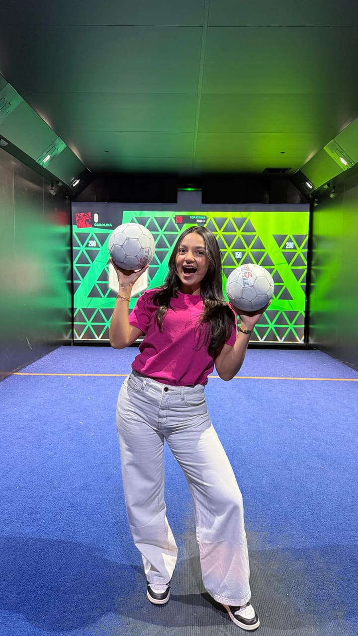 A woman showcases her experience at Toca Social, an interactive football and entertainment venue. The video features clips of her and her friends playing various virtual football games, enjoying cocktails, and eating food. The food shown includes buffalo chicken wings, mini cheeseburger sliders, and fries. The venue has a modern, dark aesthetic with neon lighting and large screens for both the games and watching live sports.