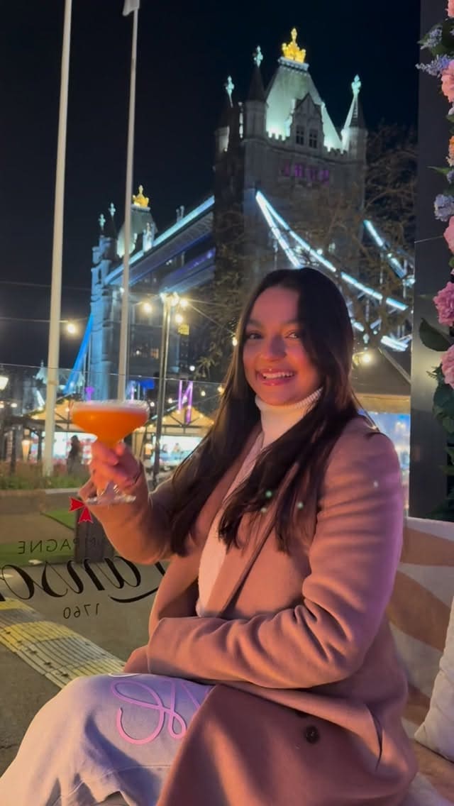 The video promotes Vicinity, a restaurant and bar in London, highlighting its prime location with views of Tower Bridge. The video showcases both the outdoor terrace with fire pits and cozy seating, and the indoor dining area. A variety of food and drinks are featured, including cocktails, fried chicken salad, crispy prawns with mango dip, nachos, a large tomahawk steak with sides of fries and mashed potatoes, and a chocolate cake with raspberry sorbet for dessert.