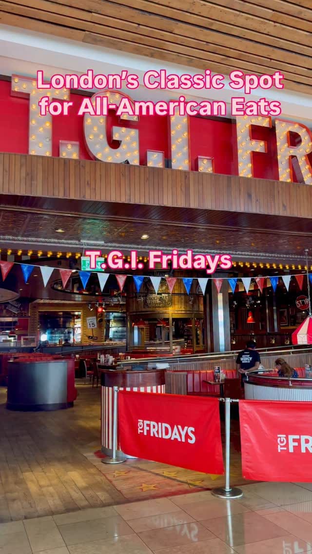 The video showcases the TGI Fridays restaurant at Westfield Stratford, London. It begins with shots of the restaurant's exterior and interior, highlighting its American diner-style decor. It then shows a group of people toasting with cocktails (a mojito and two other lime-based drinks). The main focus is on the food, featuring a variety of dishes spread across a table, including loaded nachos with guacamole and pickled onions, sesame chicken strips with fries, and a classic beef burger with fries. The video uses close-up shots to emphasize the texture and presentation of the food.