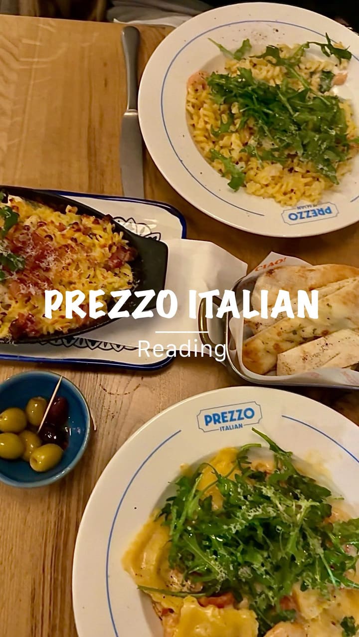 The video showcases a dining experience at Prezzo Italian restaurant in Reading. It begins with exterior shots of the restaurant, then moves inside to show the decor and ambiance. The video features a server pouring prosecco, followed by a montage of various dishes. These include hot honey glazed mozzarella sticks with a prominent cheese pull, gluten-free garlic bread, crab and lobster ravioli, chicken spaghetti carbonara (al forno), chicken mushroom garlic pasta, an affogato dessert with espresso being poured over ice cream, Nutella doughballs being dipped in chocolate sauce, and a final toast with small bottles of Pallini Limoncello. The video concludes with a night shot of the restaurant's exterior.