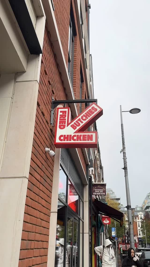 The video showcases Butchies Fried Chicken, a restaurant in London. It features various menu items, including a burger with chicken tenders and cheese sauce, chicken wings, and cheese fries. The food is presented on trays and in individual containers, highlighting the crispy textures and generous portions. The video focuses on the food's visual appeal, particularly the chicken's golden-brown color and the melted cheese. Dietary information isn't explicitly provided.