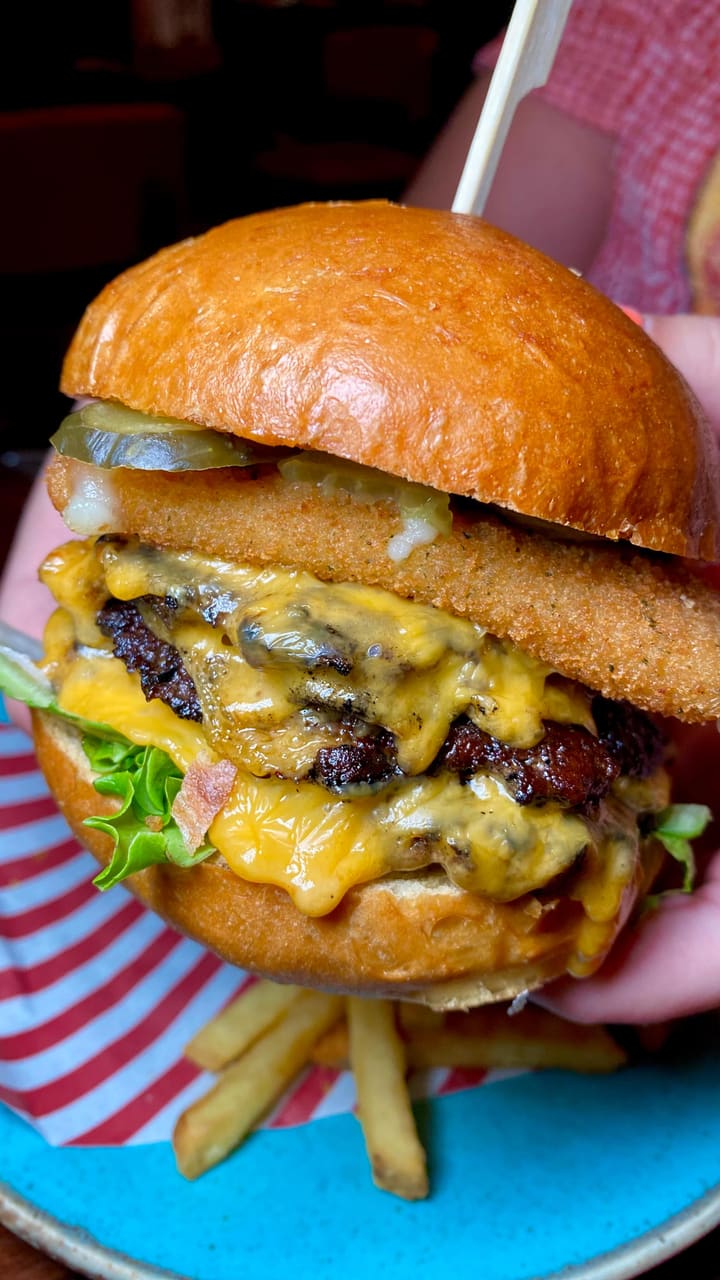 The video showcases the new menu at a TGI Fridays restaurant in Cardiff. It features several dishes: mozzarella sticks with a cheese pull, sesame chicken strips with a dipping sauce, a large multi-layered beef burger with a fried mozzarella patty, sizzling fajitas with various toppings, and a Biscoff cheesecake with caramel sauce. It also shows various cocktails, including a margarita with a chili-lime rim and other colorful drinks. The video uses quick cuts, upbeat music, and text overlays to highlight each menu item.