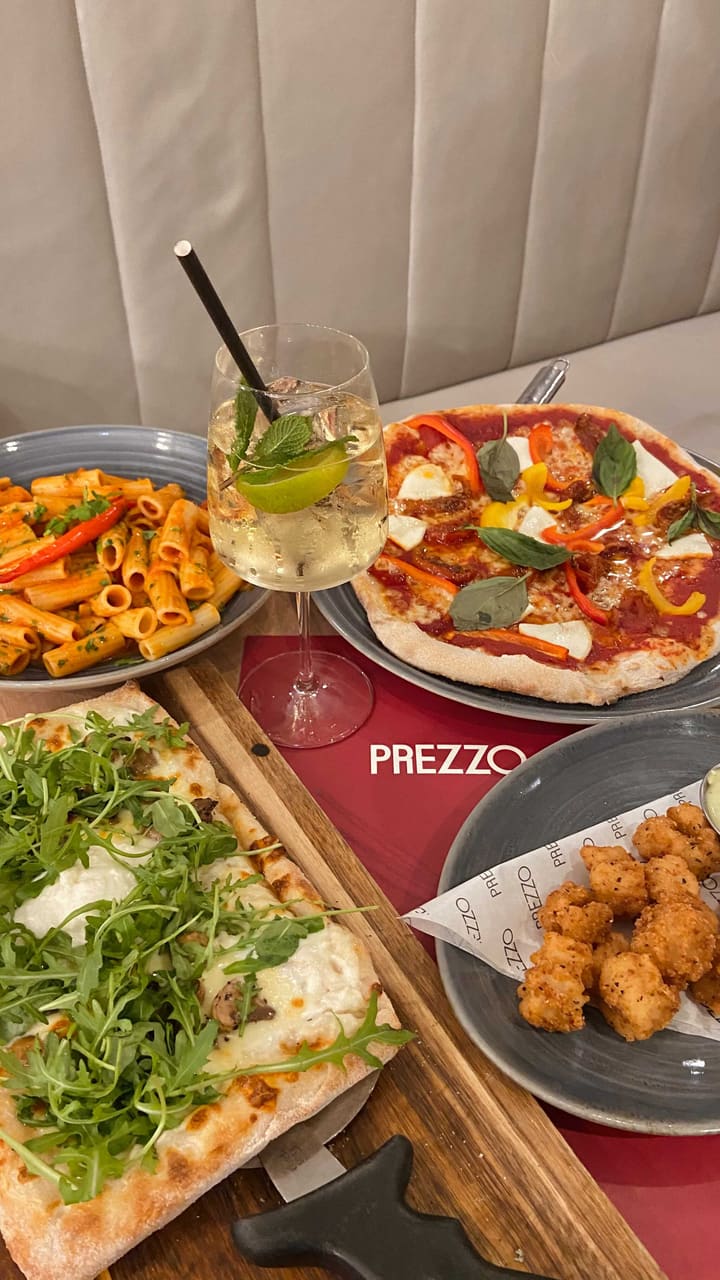 The video showcases a meal at Prezzo, an Italian restaurant. It features various dishes including pizzas (mushroom, burrata, and truffle; another with peppers), pasta (arrabbiata), fried mozzarella balls with a green sauce, cannelloni, affogato, and lemon meringue pie. The presentation is appealing with overhead shots of the pizzas, close-ups of individual dishes, and clear shots of drinks and desserts.  No specific dietary information is provided.