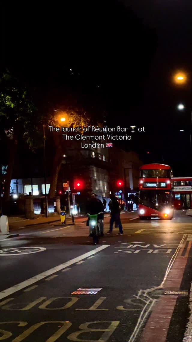The video showcases the launch event of Réunion Bar, located within The Clermont Victoria hotel in London. It begins with an exterior night shot before moving inside to display the bar's lively and sophisticated atmosphere, characterized by moody pink and red lighting. The video highlights the grand hotel interiors, including a large staircase and ornate chandeliers. It follows an influencer enjoying the event, with several scenes showing bartenders skillfully preparing and garnishing cocktails. The drinks featured include a creamy, pale yellow cocktail with a dried pineapple slice. A key feature shown is the bar's unique view overlooking the Victoria station concourse.