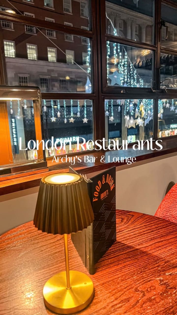 The video promotes Archy's Bar & Lounge located in The Marble Arch Hotel. It showcases the restaurant's interior, its view overlooking the Oxford Street Christmas lights, and a variety of dishes. The food items shown include arancini, crispy chicken tenders, prawns with pita bread, a Philly cheesesteak sandwich with fries, and a lemon meringue pie for dessert. The video also features two cocktails being cheersed.
